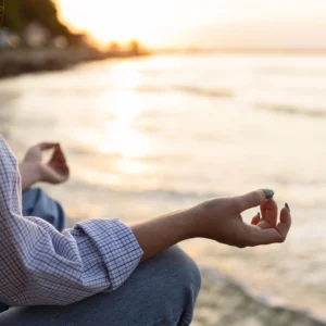 Femme méditant au bord de la mer au coucher du soleil, en position de relaxation avec les mains en mudra. Atmosphère paisible et harmonieuse, idéale pour la détente et la pleine conscience.